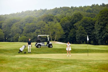 Bir çift golf sahasında birlikte eğleniyor, kahkahalarını paylaşıyor ve golf ekipmanlarını değiş tokuş ediyorlar, ki bu da oyunun saf zevkini ve heyecanını güzel bir şekilde vurguluyor.