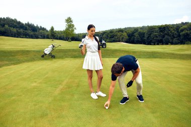 Bir çift, lüks yemyeşil bir sahada, güneşin altında ve açık mavi gökyüzünde golf oynarken güzel romantik bir anın tadını çıkarıyorlar.