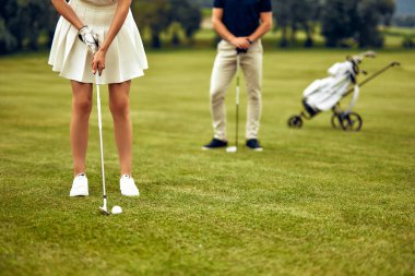 Yetenekli bir bayan golfçü, dünyanın dört bir yanındaki golf meraklıları için büyüleyici bir sahne yaratan, destekleyici eşi eşliğinde, güzel, yemyeşil bir topa dikkatlice vuruyor.