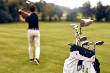 Kendini adamış bir golfçü, çok güzel, yemyeşil bir pistte tutkulu bir şekilde sallanır, kaliteli golf sopaları ön planda belirgin bir şekilde sergilenir, sporun gerçek özünü mükemmel bir şekilde gözler önüne serer.