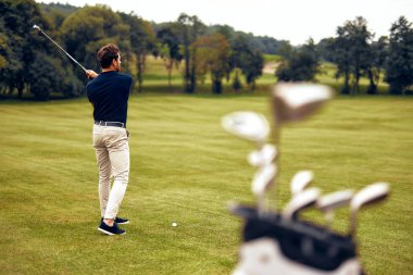 Kendini adamış bir golfçü, çok güzel, yemyeşil bir pistte tutkulu bir şekilde sallanır, kaliteli golf sopaları ön planda belirgin bir şekilde sergilenir, sporun gerçek özünü mükemmel bir şekilde gözler önüne serer.