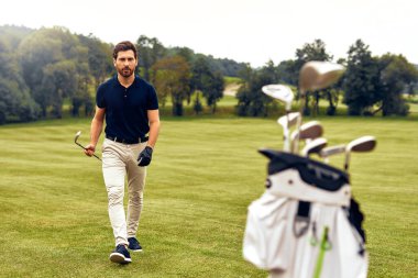 Şık bir golfçü, canlı yeşillerde güvenli adımlar atar. Heyecan ve özgüven yayar. Aynı zamanda golf sopalarını tutar, spor ve yaşam tarzının özünü somutlaştırır.