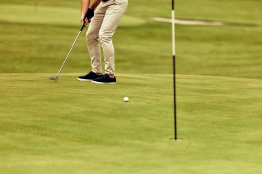 Kendini adamış bir golfçü güzel manikürlü bir yeşile vurmaya özen göstererek golfte önemli olan yoğun odaklanma ve dikkat çekici hassasiyeti gözler önüne seriyor.