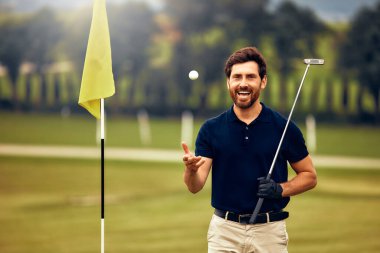 Siyah polo ve haki pantolonlu neşeli bir golfçü yeşil bayrağın yanında başarılı bir atış yaparak insanları bir araya getiren heyecanı kutluyor.