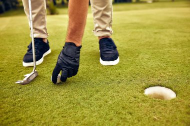 Bir golfçü golf topuna çok yakın bir golf sopasını ustalıkla yerleştiriyor, tamamen hazır ve güzel, yemyeşil bir golf sahasındaki deliğe doğru isabetli bir atış yapmaya odaklanıyor.