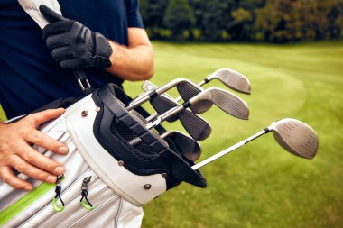 Yetenekli bir golfçü, elinde golf sopalarıyla yemyeşil alanda duruyor, heyecanlı bir güne hevesle hazırlanıyor, şık ve sportif bir görünüm sergiliyor.