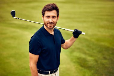 Şık ve kendinden emin bir golfçü canlı yeşil bir golf sahasında elinde golf sopasıyla gururla durur. Bu çarpıcı görüntü tüm golf meraklıları ve çeşitli spor terfileri için mükemmeldir.