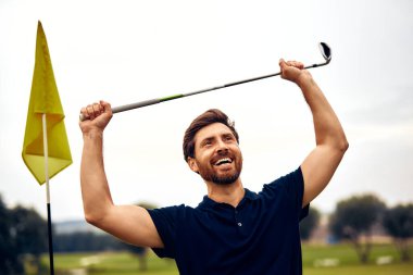 Işıldayan ve sevinçli bir golfçü, yeşil sahada başarılı bir atış yaparak, zaferin ve spordaki başarının özünü somutlaştırarak, kulübünü kutlama ve neşe içinde gururla yükseltir.