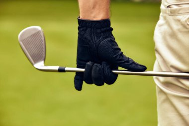 Bu görüntü, demir sopayı kavrayan bir golfçünün canlı yeşil arkaplanla güzel zıtlaşan siyah bir eldiveni göstererek görsel olarak çarpıcı bir sahne yaratmasını gösteriyor.