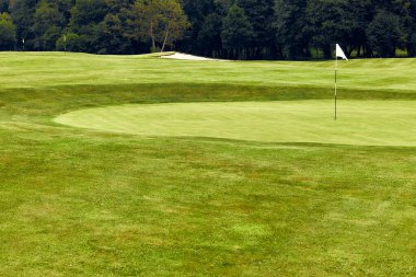 Manikürlü yeşil ve dalgalı bir bayrağı olan dingin bir golf sahası. Etrafı canlı yeşilliklerle çevrili. Hem golf meraklıları hem de doğa severler için mükemmel. Rahatlamak ve dinlenmek için ideal.