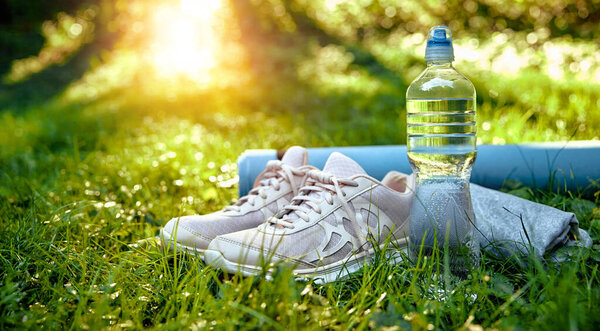 A pair of trendy and stylish running shoes, a reusable water bottle, and a neatly rolled yoga mat, all placed on vibrant lush green grass, ideal for an energizing morning workout in nature