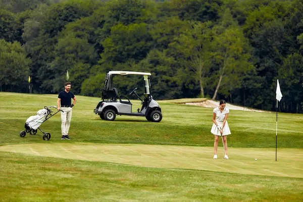 Bir adam ve bir kadın güzel korunan yemyeşil bir golf sahasında golf oynuyorlar, yakınlarda park edilmiş bir golf arabasıyla, mükemmel bir eğlence, keyif ve sportmenlik karışımı sergiliyorlar.