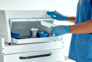 Mavi eldivenli bir sağlık çalışanı, steril ve verimli bir çalışma alanı sağlamak için klinikte tıbbi malzemeler düzenliyor ve sağlık ortamında optimal hasta bakımı ve güvenliğini sağlıyor.