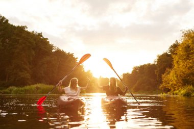 İki arkadaş birlikte keyifli bir kano macerasından zevk alıyorlar, sersemletici bir gün batımının altında ustalıkla kürek çekiyorlar, sıcaklık ve mutlulukla dolu.