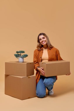 Neşeli bir atmosferde, neşeli genç bir kadın hareketliliği, ev dekorunu ve organizasyonu sembolize eden, sükuneti ve yaratıcılığı davet eden canlı bir saksı bitkisine hayran kalarak organize kutuların yanında diz çöker.