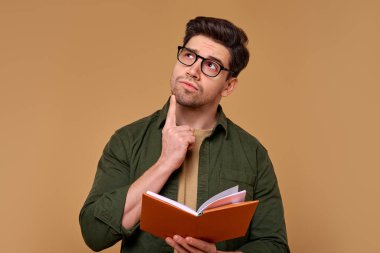 Gözlük takan genç bir adam, kendisini çevreleyen sıcak ve davetkar arka planla aydınlatılan düşünceli ve meraklı ifadesiyle bir kitap okumaya dalmışken derin derin düşünür.