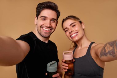 Mutlulukla dolu neşeli bir çift ellerinde geniş gülümsemeler ve su şişeleriyle antrenman sonrası anlarını yakalar. Formlarını mükemmel bir şekilde gösterirler ve sağlık hizmetlerine olan bağlılıklarını paylaşırlar.