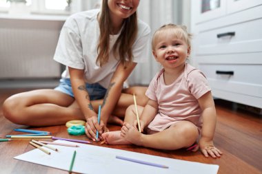 Neşeli bir anne ve küçük çocuğu evlerinde neşeli ve renkli pastel boyalarla çevrili keyifli, yaratıcı bir sanat seansına katılıyorlar.