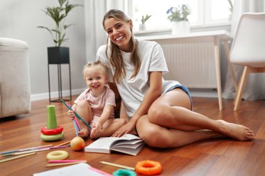 Sevgi dolu bir anne ve onun neşeli çocuğu arasında, yaratıcılıklarını ve hayal güçlerini ateşleyen renkli oyuncaklarla çevrili, sıcak ahşap bir zeminde, neşeli bir an paylaşılır.