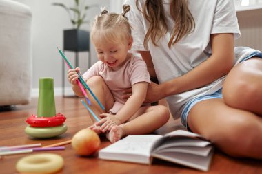Sevgi dolu bir anne ve onun neşeli çocuğu arasında, yaratıcılıklarını ve hayal güçlerini ateşleyen renkli oyuncaklarla çevrili, sıcak ahşap bir zeminde, neşeli bir an paylaşılır.