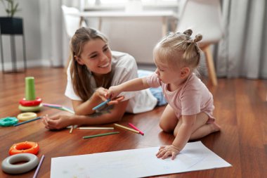 Neşeli bir anne ve küçük çocuğu evlerinde neşeli ve renkli pastel boyalarla çevrili keyifli, yaratıcı bir sanat seansına katılıyorlar.