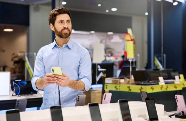 Mobil aksesuarlarla dolu hareketli bir perakende mağazasında, bir adam kendini akıllı telefonların çeşitli özelliklerini keşfetmeye kaptırırken, bir yandan da modern teknoloji aletleri ve vitrinlerle çevrili...