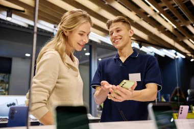 Müşteri, çeşitli teknolojilerle dolu canlı ve dinamik bir perakende ortamında çeşitli akıllı telefon seçeneklerini ayrıntılı bir şekilde incelerken bilgili bir satıcıya danışmanlık yapmaktadır.