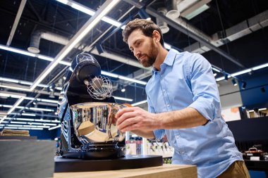 Bir adam, perakende mağazası için tasarlanmış ve potansiyel alıcılara çeşitli özelliklerini, işlevlerini ve parlak tasarımlarını gösteren çağdaş bir stand mikserle meşgul oluyor.