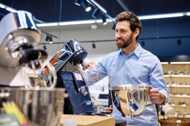 Bir adam, perakende mağazası için tasarlanmış ve potansiyel alıcılara çeşitli özelliklerini, işlevlerini ve parlak tasarımlarını gösteren çağdaş bir stand mikserle meşgul oluyor.