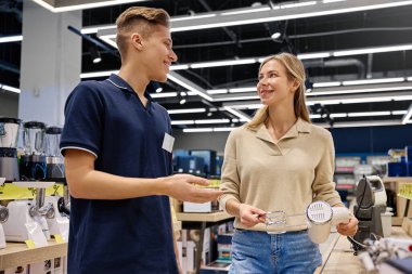 Modern bir perakende mağazasında bir satış elemanı ile bir müşteri arasında sıcak ve dostane bir alışveriş gerçekleşir. Bu alışveriş, mükemmel müşteri hizmetleri ve nişanlanmanın özelliklerini zekice gözler önüne serer.