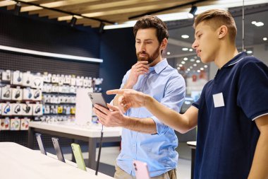 Modern bir perakende satış ortamında, müşteri en son akıllı telefonlar hakkında bilgili bir satıcıya hevesle konuşur ve etkileşim sırasında kişiselleştirilmiş servisin değerini vurgular.