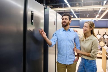 Neşeli bir çift çağdaş bir mağazada sergilenen çeşitli şık buzdolaplarını rahatça keşfediyor, çeşitli özellikleri incelemek ve düşünceli bir şekilde birlikte karar vermek için zaman harcıyor.