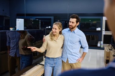 Neşeli bir çift, modern bir elektronik mağazasında bulunan geniş bir televizyon yelpazesini mutlulukla keşfeder. Bu eğlenceli gezintide yoldaşlıklarını, heyecanlarını ve ortak ilgi alanlarını sergilerler.