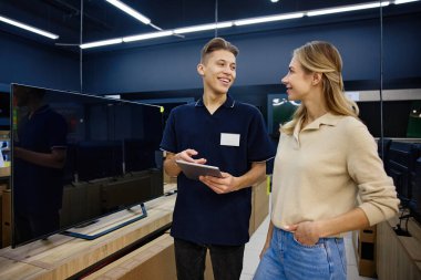 Çalışkan bir teknoloji mağazasında parlak ve neşeli bir etkileşimde, bilgili bir satıcı çeşitli televizyonlarda yardım arayan meraklı bir müşteriye uzman rehberliği sunar.