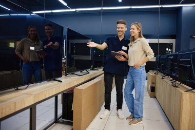 Çalışkan bir teknoloji mağazasında parlak ve neşeli bir etkileşimde, bilgili bir satıcı çeşitli televizyonlarda yardım arayan meraklı bir müşteriye uzman rehberliği sunar.