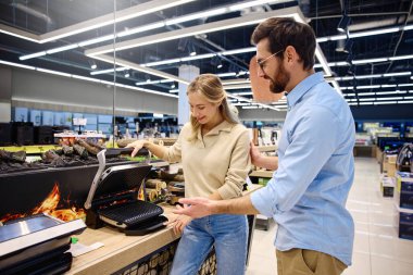 Modern ve iyi aydınlatılmış bir perakende mağazasında, neşeli bir çift, seçeneklerini keşfederken farklı mutfak aletleriyle coşkuyla etkileşime geçer, gülümseyerek ve birlikte eğlenerek.