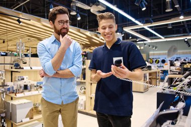 Çağdaş bir perakende satış ortamında, bir müşteri bir mağaza çalışanı ile alışverişe hazır çeşitli elektronik cihazları araştırırken sohbet eder.