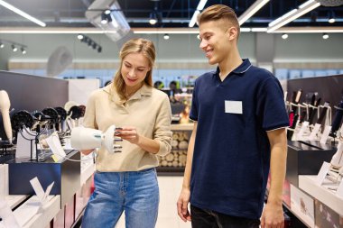 Parlak, modern bir mağaza ortamında bilgili bir satıcıyla saç şekillendirme aletlerini keşfeden mutlu bir müşteri.