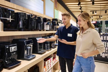 Yetenekli bir satıcı, çağdaş bir perakende mağazasında çeşitli kahve makineleri sergileyerek, mevcut özellikleri, faydaları ve çeşitli seçenekleri ayrıntılı bir şekilde ön plana çıkarıyor.