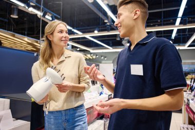 Parlak, modern bir mağaza ortamında bilgili bir satıcıyla saç şekillendirme aletlerini keşfeden mutlu bir müşteri.