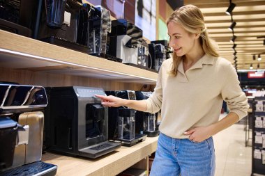 Genç bir kadın, daha iyi bir kahve yapma deneyimi için kaliteli demleme çözümleri ve yenilikçi aletlere olan ilgisini gösteren, perakende satış mağazalarını heyecanlı bir şekilde keşfediyor.