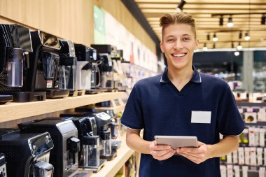 Yoğun bir elektronik reyonunda, modern bir tabletle hevesli bir ortak, müşterilerine evleri için alışveriş yaparken ihtiyaçlarına uygun mutfak aletleri bulmalarında yardımcı olmaya hevesli.