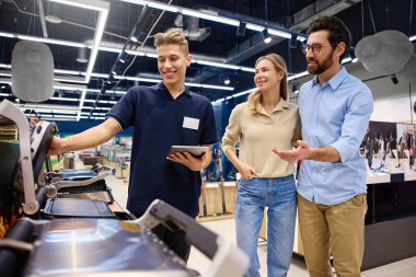 En son teknolojiye sahip modern bir perakende mağazasında, bilgili bir satış görevlisi, bir çiftin uygun alımlar hakkında dostça ve bilgilendirici bir tartışma yaparak elektroniği keşfetmesine yardımcı oluyor.