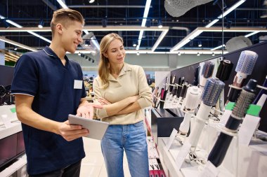 Parlak, modern bir mağaza ortamında bilgili bir satıcıyla saç şekillendirme aletlerini keşfeden mutlu bir müşteri.