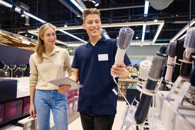 Parlak, modern bir mağaza ortamında bilgili bir satıcıyla saç şekillendirme aletlerini keşfeden mutlu bir müşteri.