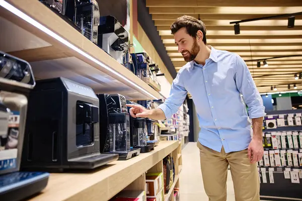 Bir adam, modern bir mağazada sergilenen çeşitli kahve makinelerini inceliyor ve inceliyor, yaklaşan alışverişi ve ihtiyaçlarına en uygun olan şeyleri inceliyor.