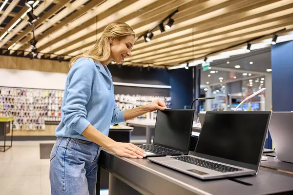 Parlak bir elektronik mağazasında, bir kadın en son teknoloji ve yenilikçi aletlerle birlikte, dinamik bir yaşam tarzı için çeşitli ürünlerle geliştirilmiş dizüstü bilgisayarları zevkle keşfeder.
