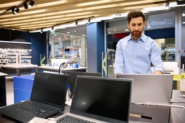Moda bir elektronik butikte, genç bir adam çeşitli dizüstü bilgisayarları hevesle araştırıyor, modern teknolojiyi gözler önüne seriyor ve onların yenilikçi özellikleri ve işlevsellikleri için heyecanını dile getiriyor.