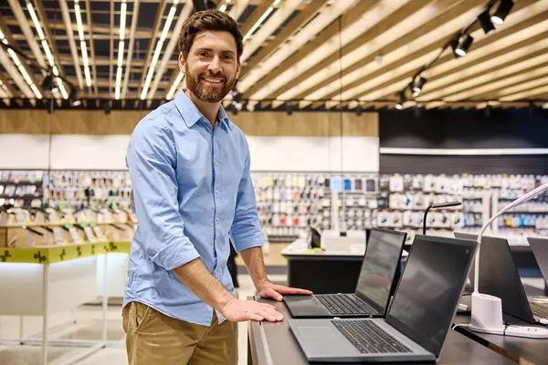 Moda bir elektronik butikte, genç bir adam çeşitli dizüstü bilgisayarları hevesle araştırıyor, modern teknolojiyi gözler önüne seriyor ve onların yenilikçi özellikleri ve işlevsellikleri için heyecanını dile getiriyor.