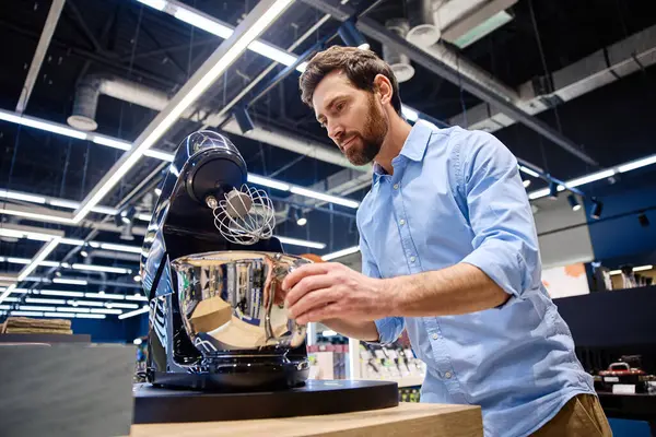 Bir adam, perakende mağazası için tasarlanmış ve potansiyel alıcılara çeşitli özelliklerini, işlevlerini ve parlak tasarımlarını gösteren çağdaş bir stand mikserle meşgul oluyor.